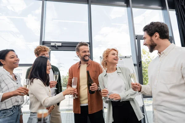 Gente de negocios multicultural feliz con copas de champán hablando durante la fiesta corporativa - foto de stock