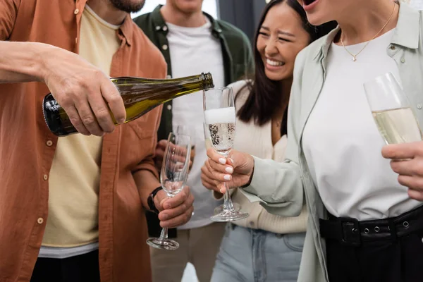 Збуджена азіатська бізнес-леді сміється біля колег, що поливають шампанське на корпоративній вечірці — стокове фото