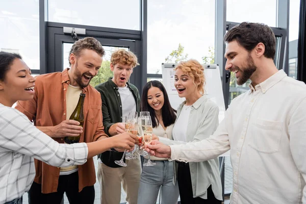 Excited multiethnic business people clinking champagne glasses during corporate party in office — Stock Photo