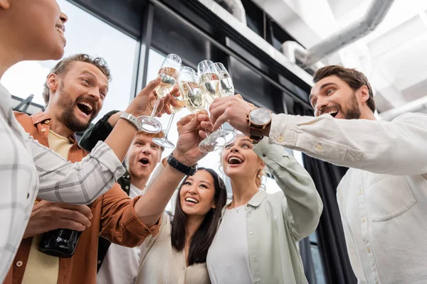Низкий угол обзора веселых деловых людей, звонящих бокалы шампанского во время корпоративной вечеринки — стоковое фото