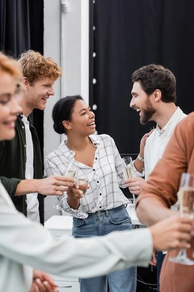 Sonriendo gente de negocios multiétnicos hablando y sosteniendo champán durante la fiesta corporativa - foto de stock