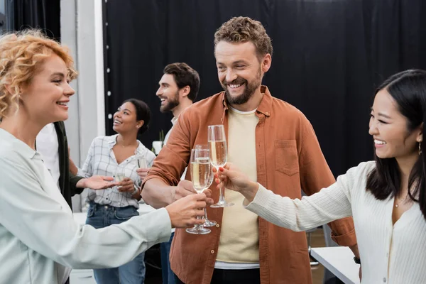 Fröhliche interrassische Geschäftsleute stoßen an und halten Champagner im Büro — Stockfoto
