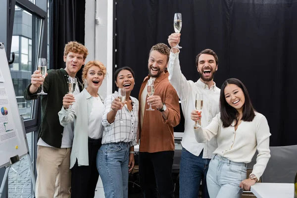 Des gens d'affaires multiculturels excités montent des verres de champagne au bureau — Photo de stock