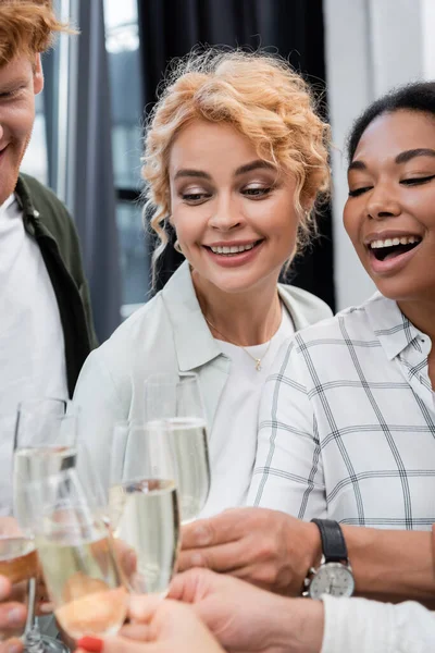 Empresária positiva clinking champanhe com colegas inter-raciais durante festa corporativa no escritório — Fotografia de Stock