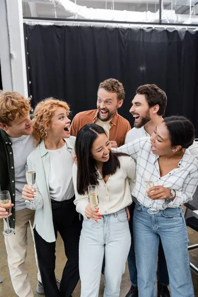 Multicultural business people hugging and holding glasses of champagne in office — Stock Photo