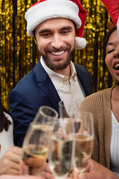 Uomo d'affari sorridente in cappello di Babbo Natale clinking champagne con uomini d'affari multietnici — Foto stock