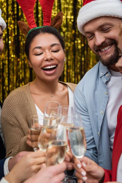Fröhliche multiethnische Geschäftsfrau mit weihnachtlichem Stirnband klappert mit Amtskollegen Champagner — Stockfoto