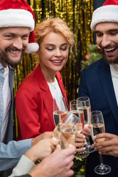 Geschäftsfrau klappert im Büro mit lächelnden interrassischen Kollegen in Weihnachtsmänteln Champagner — Stockfoto