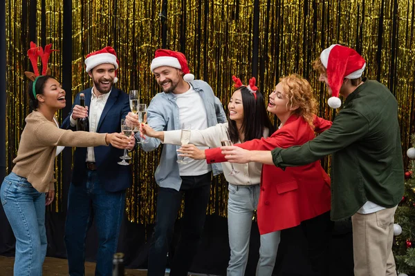 Multikulturelle Geschäftsleute mit weihnachtlichen Stirnbändern klirren neben Lametta im Büro mit Champagner — Stockfoto