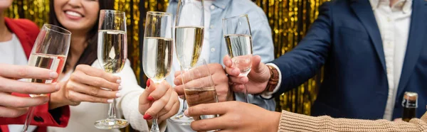 Обрізаний вид на багатоетнічних бізнесменів, які тримають келихи шампанського біля мішури в офісі, банер — стокове фото