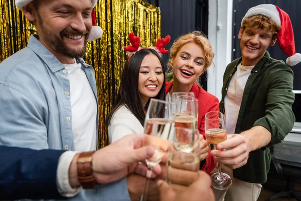 Glückliche exotische Geschäftsleute in Weihnachtsmännern stoßen bei einer Firmenparty im Büro mit Champagner an — Stockfoto