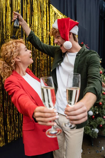 Seitenansicht des Geschäftsmannes mit Weihnachtsmannhut mit Flasche und Glas Champagner in der Nähe der Geschäftsfrau im Amt — Stockfoto
