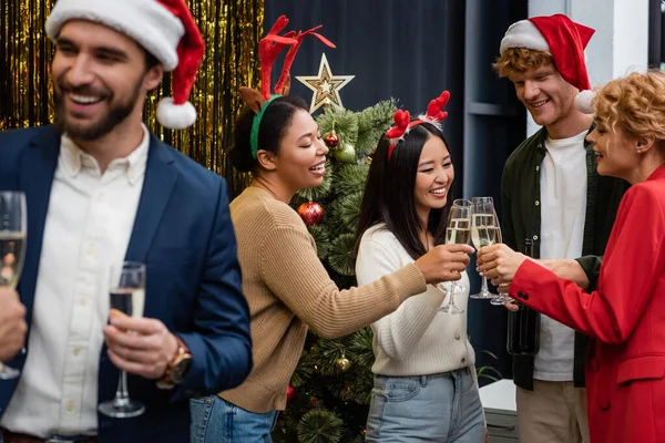 Negócios multiculturais pessoas clinking champanhe perto da árvore de Natal no escritório — Fotografia de Stock