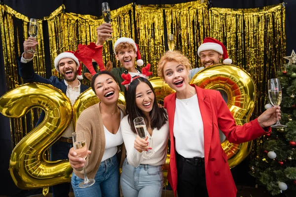 Empresarias interraciales celebrando champán cerca de empresarios y globos en forma de 2023 números en el cargo - foto de stock