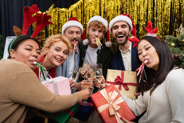 Pessoas de negócios multiculturais com chifres de festa segurando presentes e champanhe durante a festa corporativa de Ano Novo — Fotografia de Stock