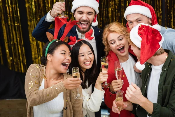 Мультиэтнические бизнесмены держат шампанское под конфетти во время рождественской вечеринки в офисе — стоковое фото