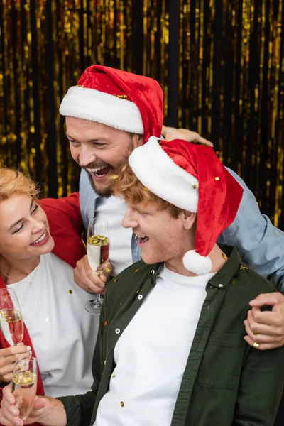Homme d'affaires dans le chapeau santa embrasser ses collègues avec du champagne pendant la fête de Noël au bureau — Photo de stock