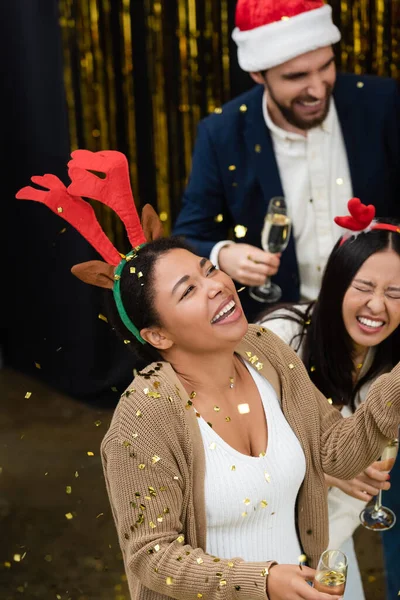 Высокий угол обзора многорасовой предпринимательницы, держащей шампанское под конфетти во время рождественской вечеринки в офисе — стоковое фото