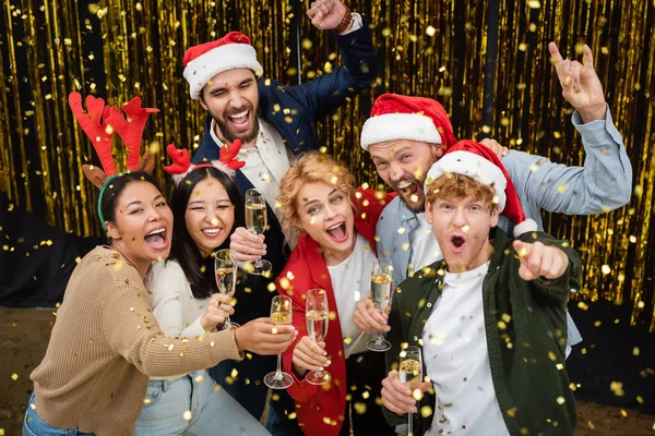 Negocios multiétnicos positivos celebrando champán bajo confeti cayendo en el cargo - foto de stock