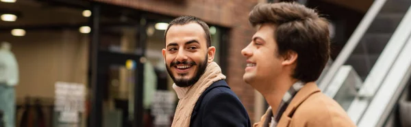 Щасливий бородатий гей чоловік дивиться на розмитого хлопця на міській вулиці, банер — стокове фото