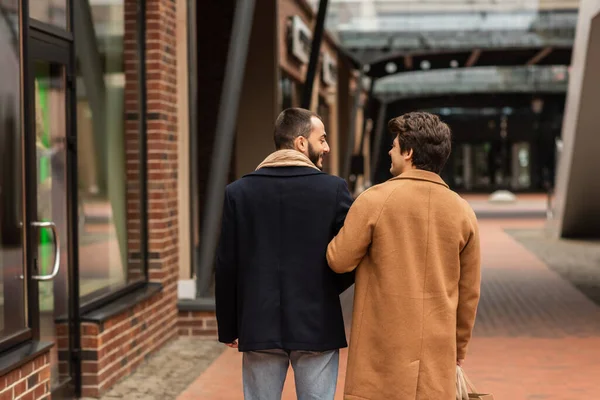 Back view of happy gay couple with shopping bags walking in city — Stock Photo