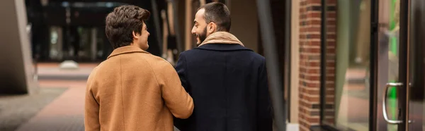 Vista trasera de la elegante pareja gay sonriendo el uno al otro en la calle urbana, pancarta - foto de stock