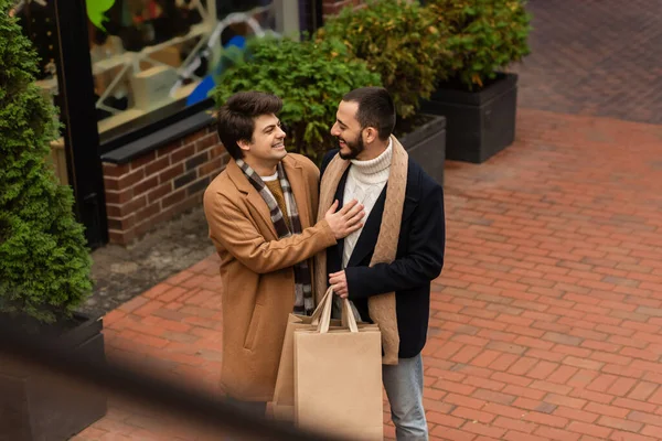 High angle view of gay man laughing near bearded boyfriend with shopping bags on urban street — Stock Photo