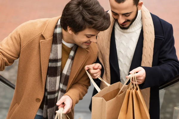 Pleased gay couple in fashionable clothes looking into shopping bag outdoors — Stock Photo