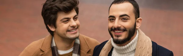 Cheerful man in braces looking at bearded gay partner outdoors, banner — Stock Photo