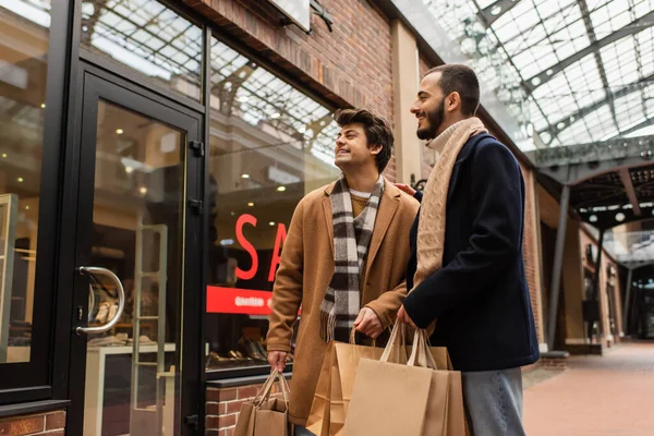 Sourire gay couple avec shopping sacs regarder vitrine sur urbain rue — Photo de stock