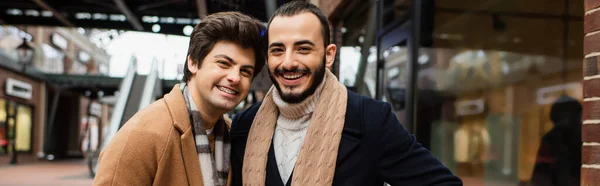 Радісні гей-партнери в шарфах і пальто дивиться на камеру на міській вулиці, банер — Stock Photo