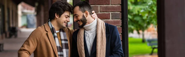 Smiling gay couple in trendy coats and scarfs standing face to face with closed eyes outdoors, banner — Stock Photo