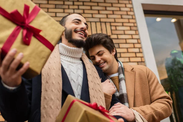 Низкий угол зрения бородатый гей держит подарочные коробки рядом счастливый парень с закрытыми глазами на улице — стоковое фото