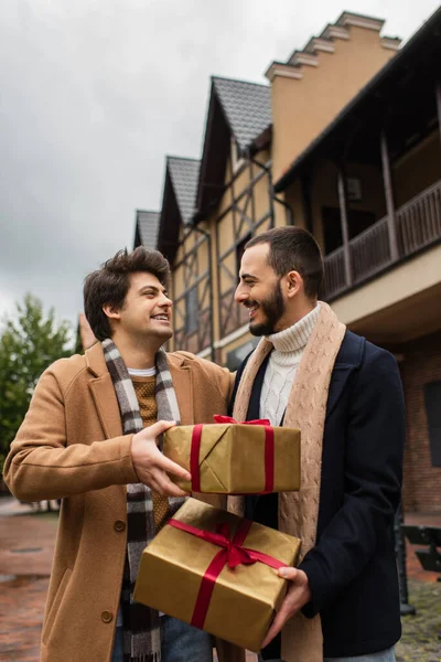Счастливая гей-пара в стильной одежде с рождественскими подарками на городской улице — стоковое фото