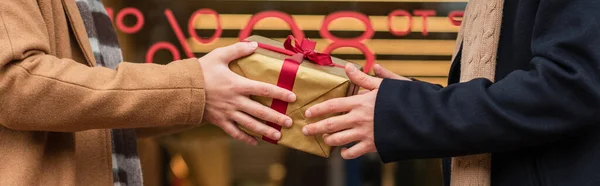Partial view of gay men holding gift box near blurred showcase, banner — Stock Photo