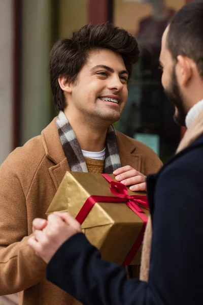 Young gay in dental braces holding hands with blurred boyfriend near Christmas present — Stock Photo
