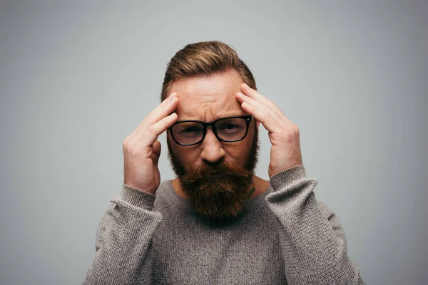 Стрессовый мужчина в очках смотрит в камеру, касаясь лба, изолированного на сером — стоковое фото