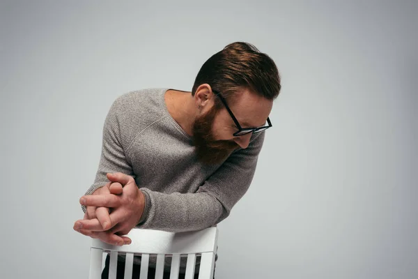 Homem barbudo em óculos olhando para longe enquanto estava perto da cadeira isolado em cinza — Fotografia de Stock