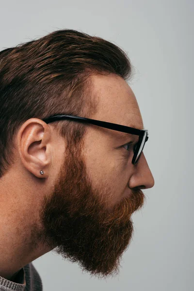 Vue latérale de l'homme barbu à lunettes regardant loin isolé sur gris — Photo de stock