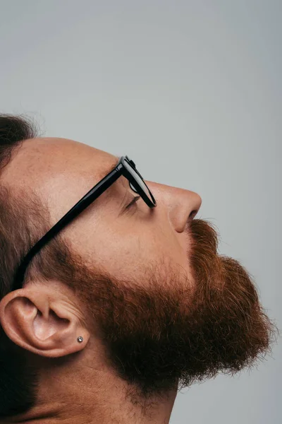 Seitenansicht eines bärtigen Mannes mit Brille, der das Auge isoliert auf Grau schließt — Stockfoto