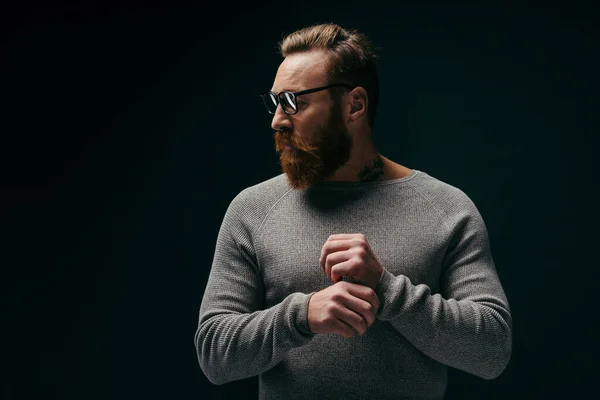 Uomo alla moda in maglione e occhiali guardando lontano isolato su nero — Foto stock