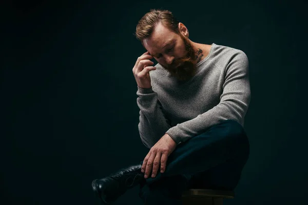 Fashionable bearded and tattooed man posing while sitting on chair isolated on black — Stock Photo
