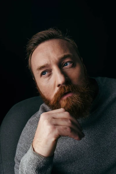 Портрет бородатого чоловіка в светрі сидить на кріслі ізольованому на чорному — стокове фото
