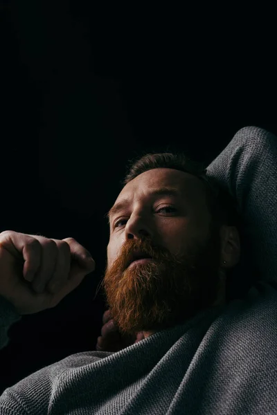 Low angle view of stylish bearded man in jumper looking at camera isolated on black with shadow — Stock Photo