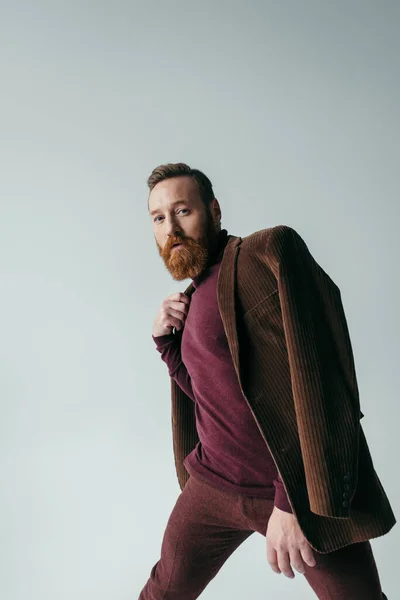 Bearded man in turtleneck and brown blazer looking at camera isolated on grey — Stock Photo