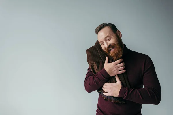 Bearded man in turtleneck embracing blazer and smiling isolated on grey — Stock Photo
