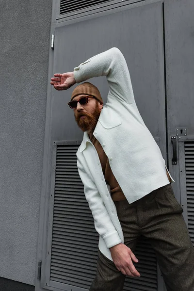 Homem elegante em chapéu de gorro e óculos de sol de pé em jaqueta de camisa branca e posando fora — Fotografia de Stock