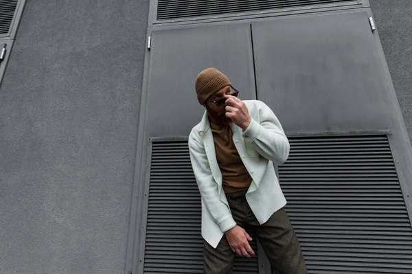 Stylish man in beanie hat and white shirt jacket adjusting sunglasses outside — Stock Photo