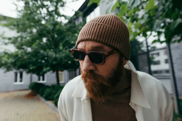 Homme suspect avec barbe dans des lunettes de soleil élégantes et bonnet chapeau — Photo de stock
