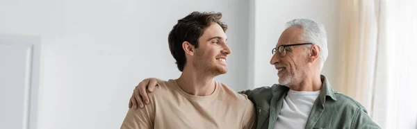 Young and happy man looking at senior father embracing his shoulders, banner — Stock Photo